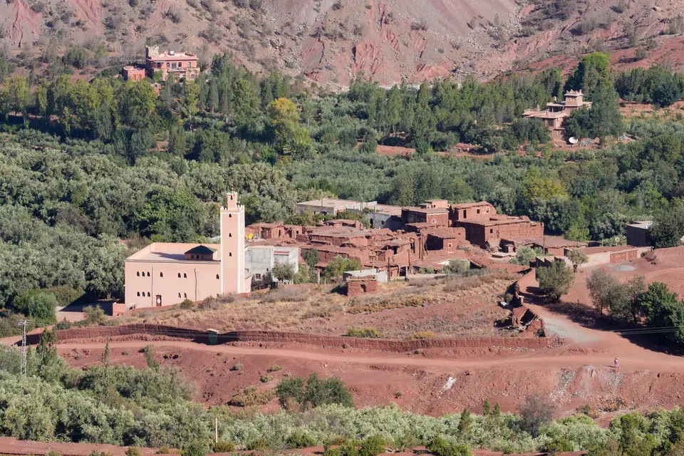 Mosquée blanche et maisons en terre du village d'Anraz, entre oliviers et collines rouges